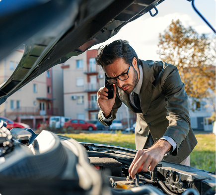 Mężczyzna w garniturze diagnozujący usterkę pod maską w trakcie rozmowy telefonicznej