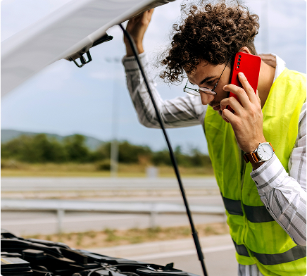 Mężczyzna w kamizelce diagnozujący usterkę pod maską w trakcie rozmowy telefonicznej