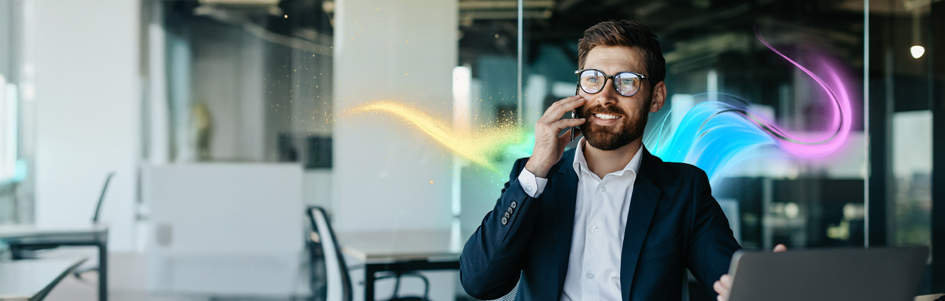 Uśmiechnięty mężczyzna w garniturze siedzi w biurze i rozmawia przez telefon.