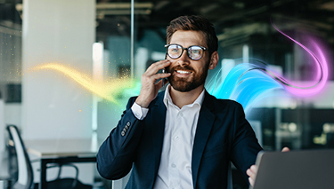 Uśmiechnięty mężczyzna w garniturze siedzi w biurze i rozmawia przez telefon.