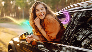 Kobieta wychylającą się z okna samochodu. W tle drzewa i droga.