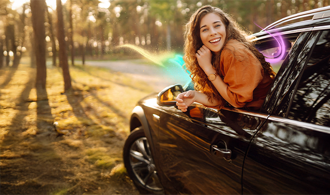 Kobieta wychylającą się z okna samochodu. W tle drzewa i droga.