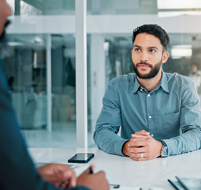 Mężczyzna w koszulki siedzący przy stole rozmawiający z innym mężczyzną.