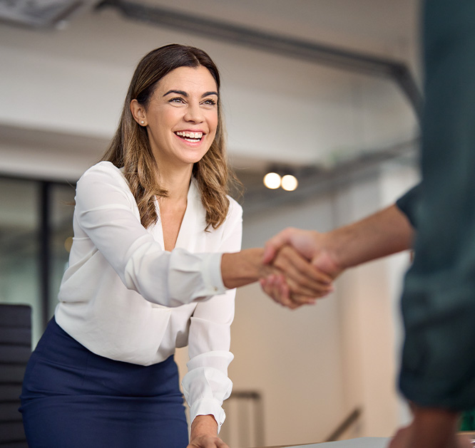Obraz przedstawiający uśmiechniętą kobietę która ściska dłoń mężczyzny. Sylwetki mężczyzny nie widać na obrazku, tylko dłoń.