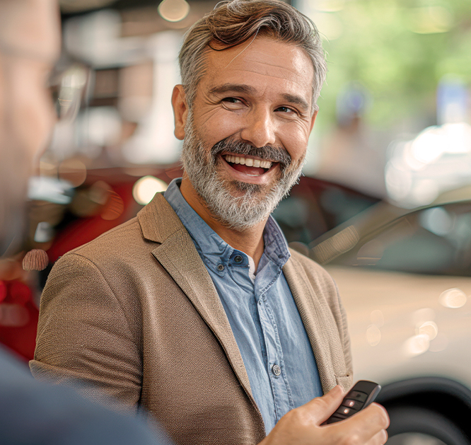 Obraz zawierający uśmiechającego się mężczyznę. W tle samochody