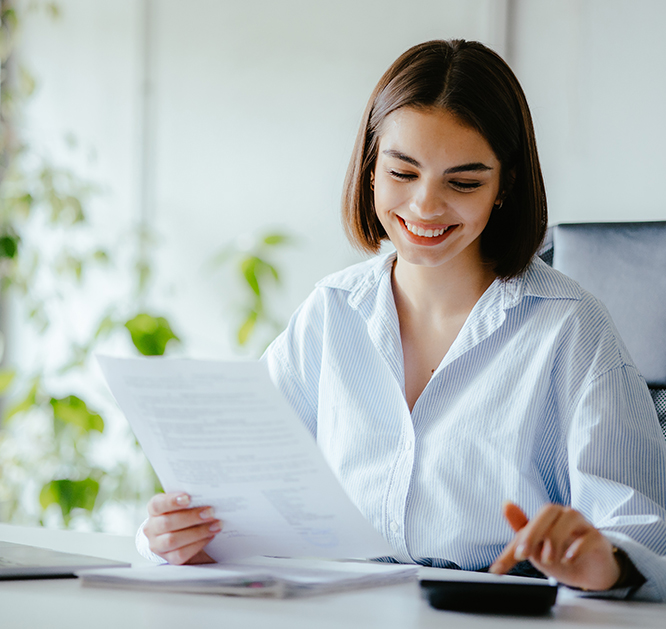 Uśmiechnięta kobieta trzymająca dokumenty w dłoni. Znajduje się z biurze.