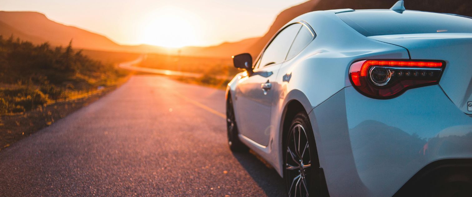 Białe sportowe auto jadące pustą drogą, w tle zachód słońca i góry