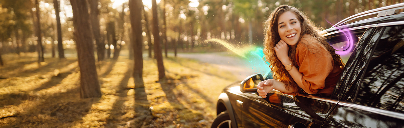 Kobieta wychylającą się z okna samochodu. W tle drzewa i droga.