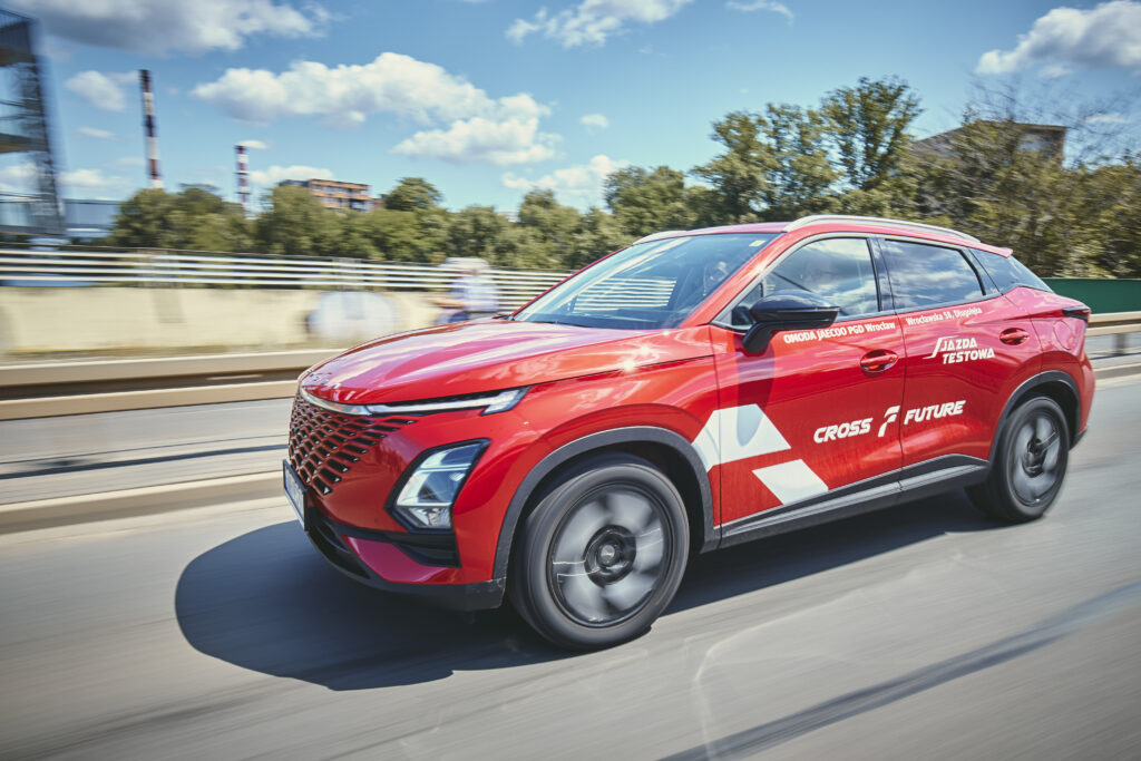 Czerwone auto marki OMODA jedzie ulicą w pogodny dzień