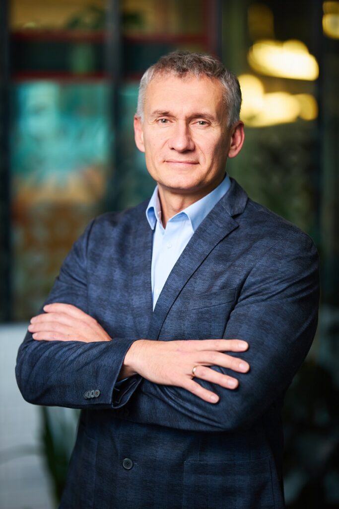 Starszy mężczyzna w garniturze patrzący w kamerę z założonymi rękami