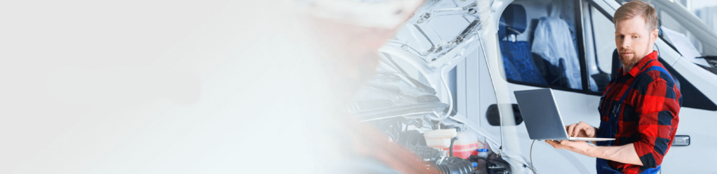 Mechanik trzyma laptopa, stoi obok samochodu z otwartą klapą.