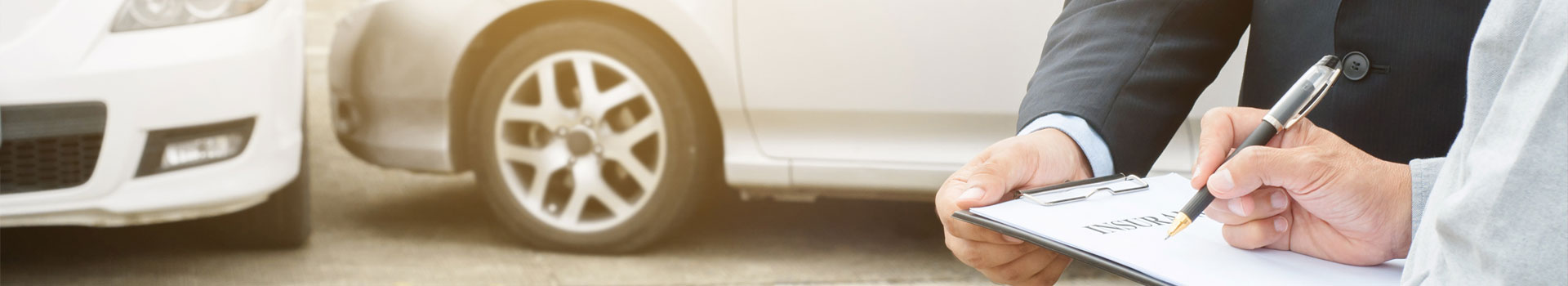 Mężczyzna w garniturze trzyma podkładkę z dokumentami podpisanymi 'Insurance'. Mężczyzna w koszuli podpisuje dokument.