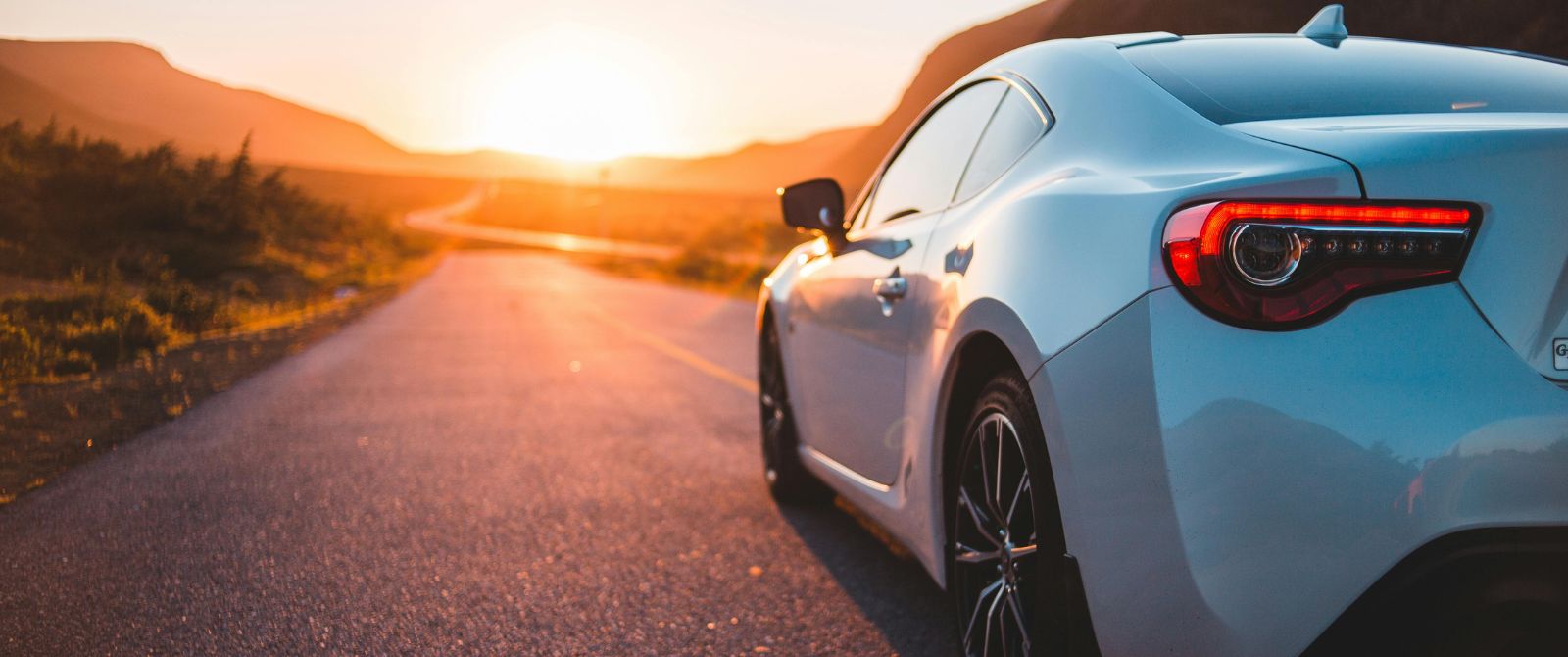 biały samochod poruszający się w stronę zachodzącego słońca